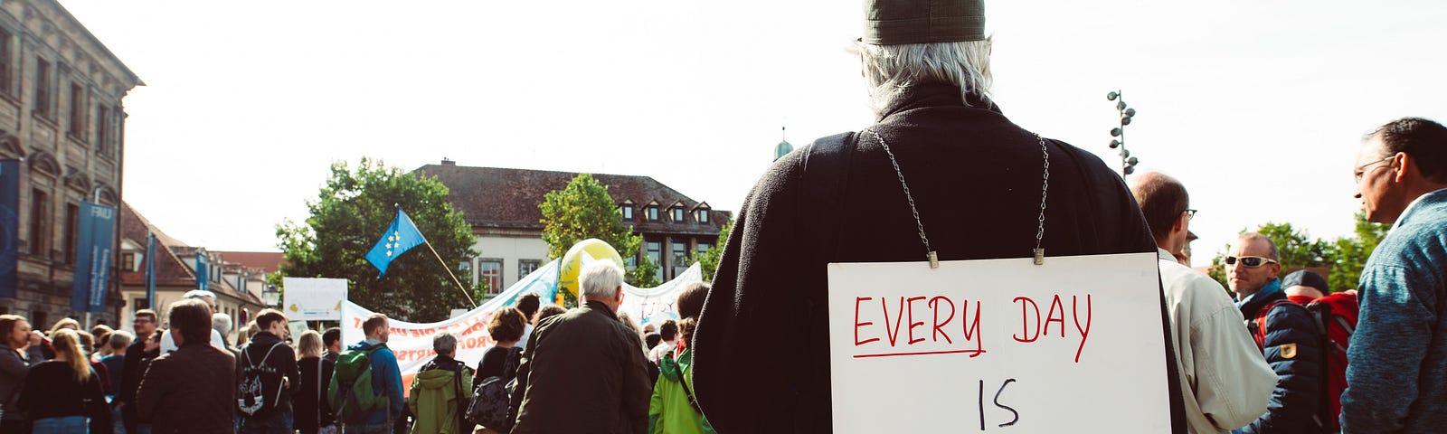 An old man holding a placard that says everyday is the future.