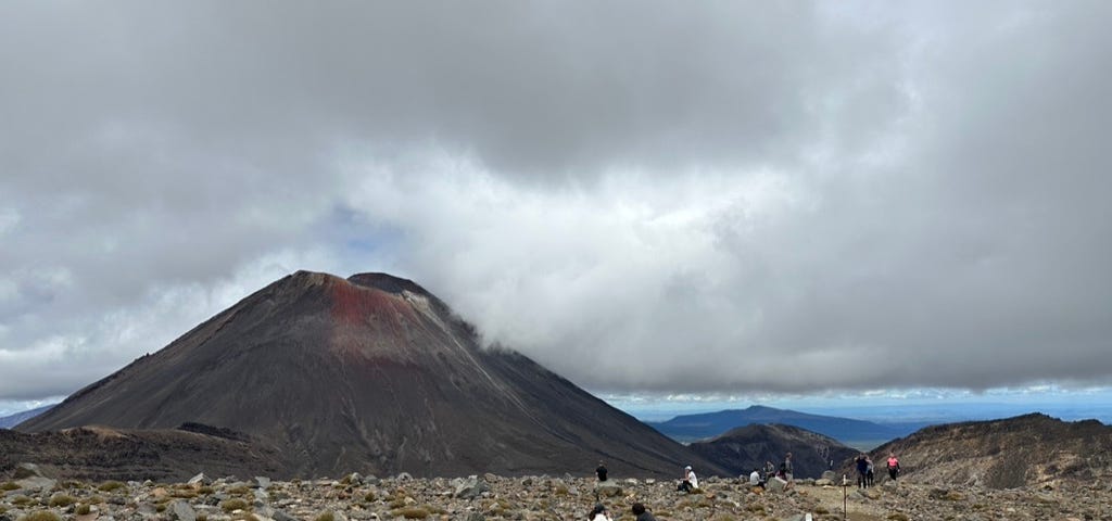 View of volcano with rocks in foreground and people dotted around.