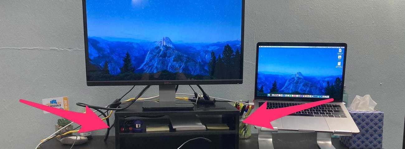 A monitor stand, laptop and keyboard desk setup.