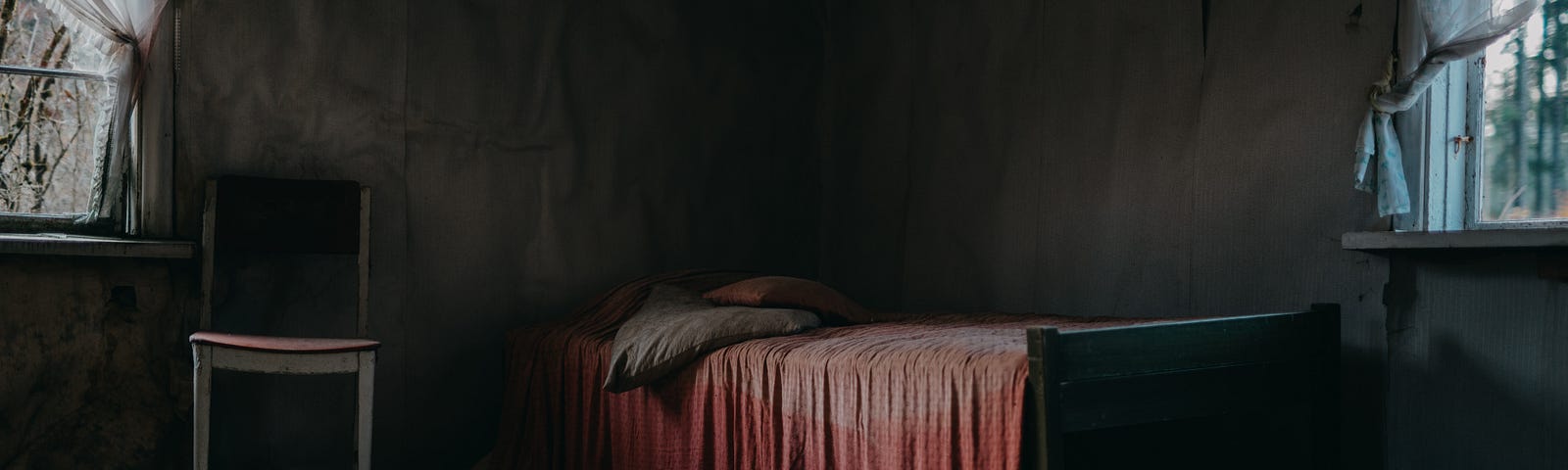 Empty room with bare floorboard and a bed with an old red blanket over the top.