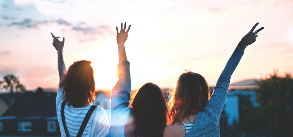 Three ladies enjoying the sunset with hands in the air.