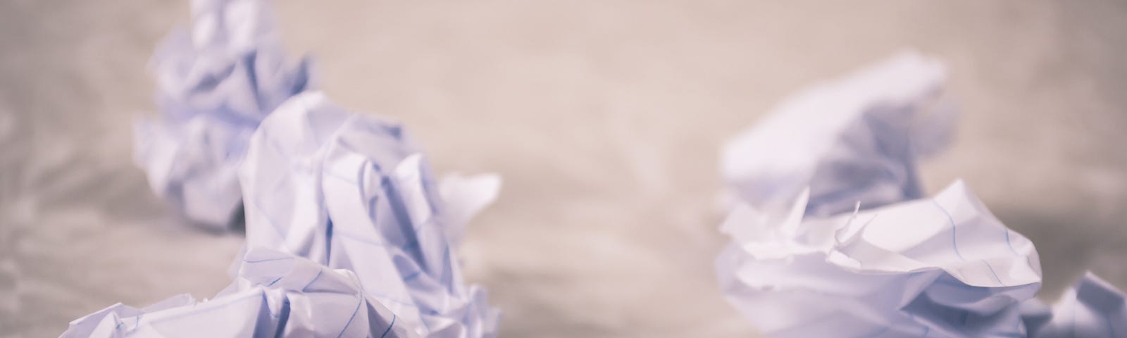 Image of a notepad with a blank page and crumpled balls of paper around it.