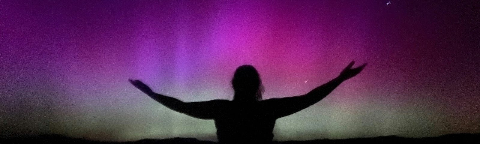 Person with outstretched arms silhouetted against the Northern Lights