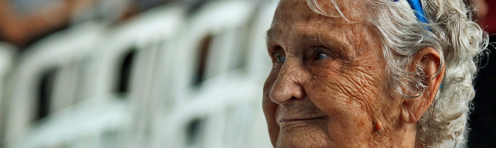 An elderly lady with a blue bow in her hair, looking off to her right.