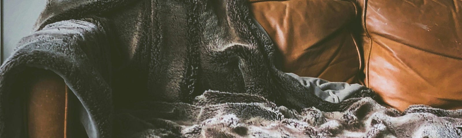 Blanket draped over light brown leather sofa.