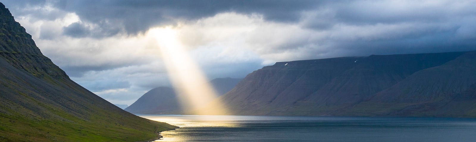 Sunlight beaming through opening in cloud cover, onto water in a bay.