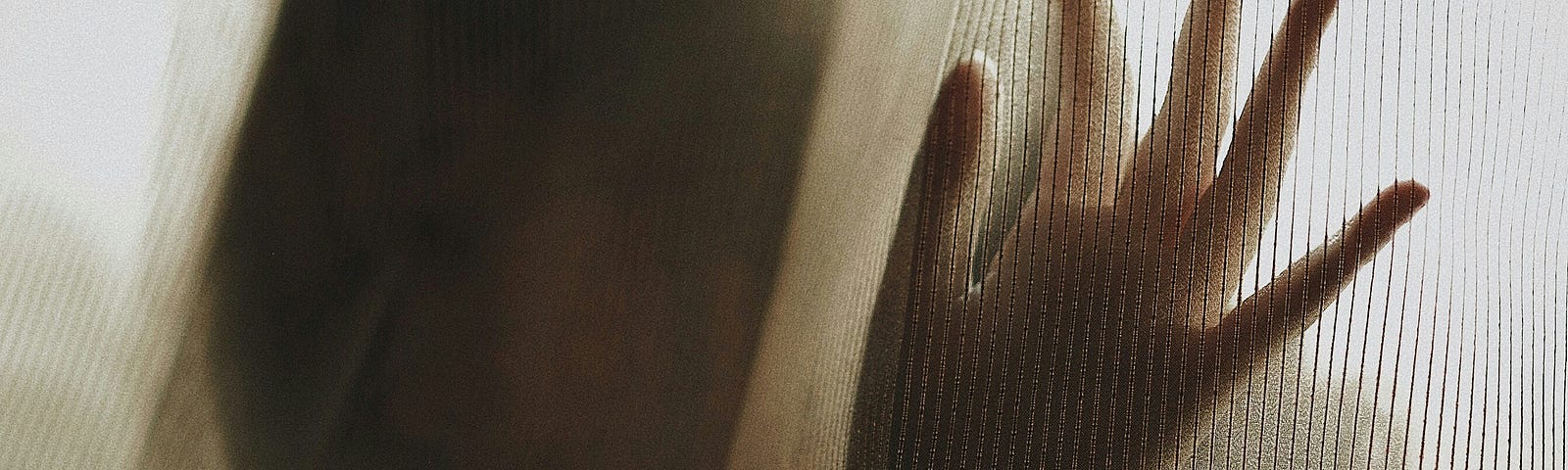 Sepia toned image of women with hand touching curtain, the image of her seen only shadow-like through the material.