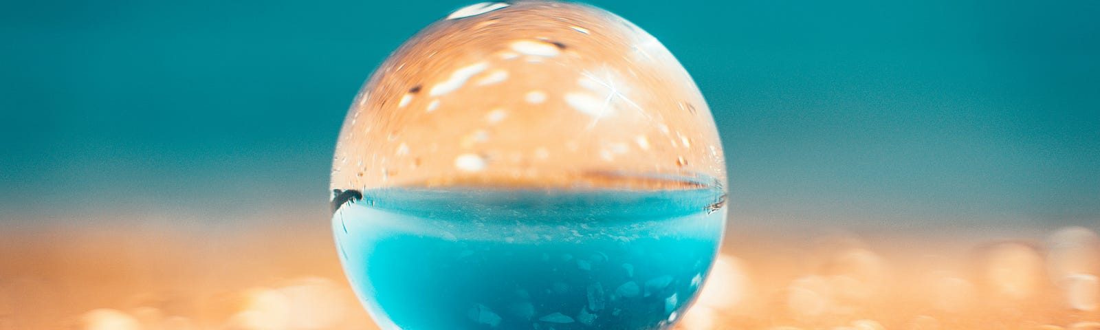 A transparent sphere reflecting the sand and ocean behind it