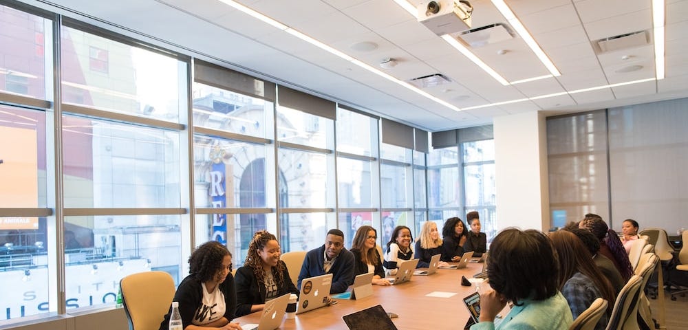 Photo of diverse employees sitting around a conference table with laptop computers during a business meeting.