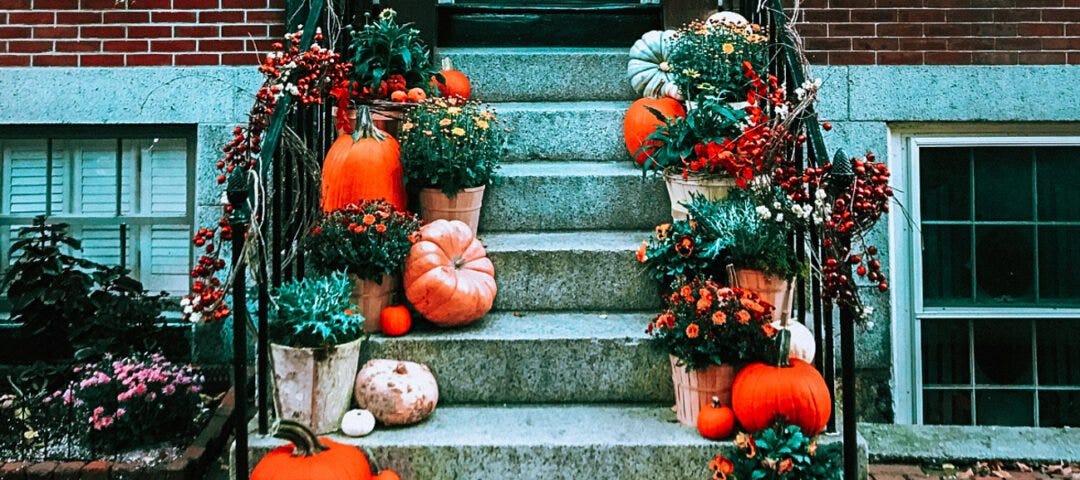 The outdoor front stairs of a house decorated with natural leaves and pumpkins
