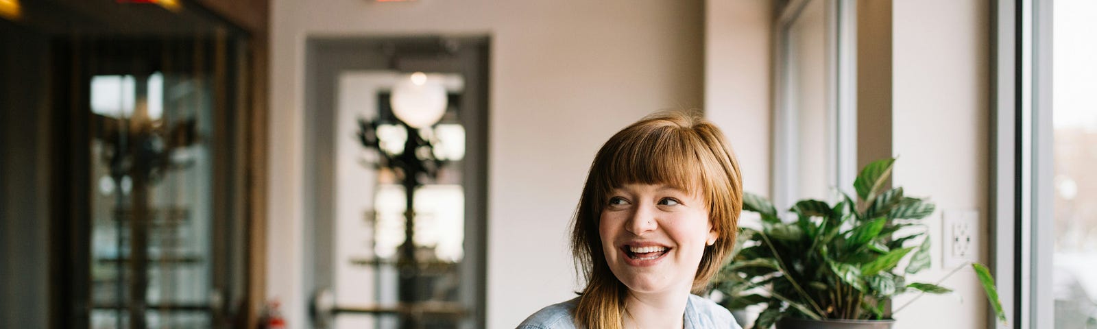 A photo of a young woman sitting in a well-lit room. Through gratitude, she has received healing from depression after years of oppression. A Journey that took her from Darkness to Joy. She has a smile and peace about her.