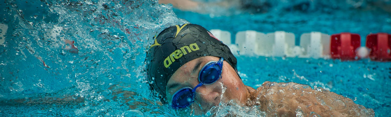 Swimmer in pool, on side, wearing a black swim cap and blue goggles.
