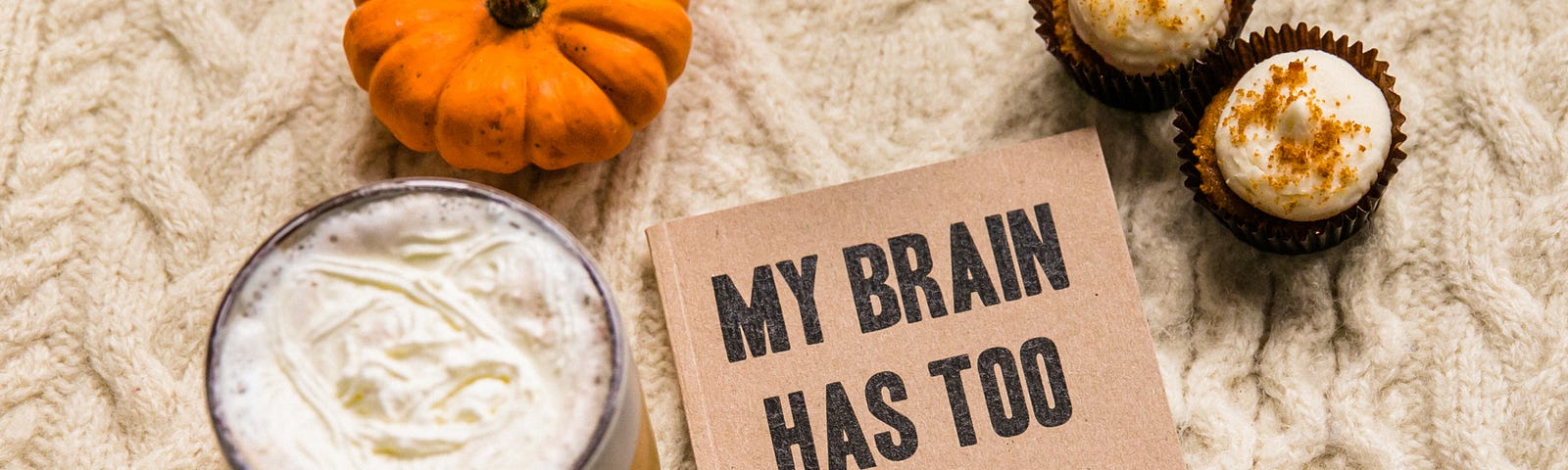 Card saying “My brain has too many tabs open” next to a cup of coffee, a small blanket, and two sweet treats.