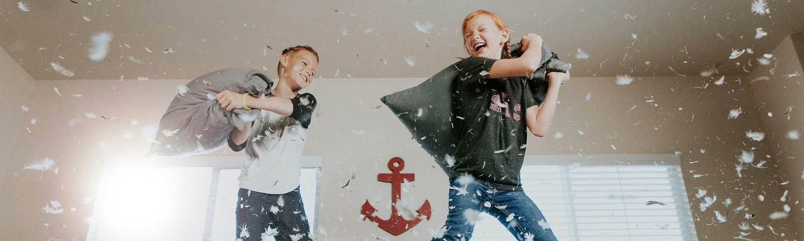 Two young boys engaged in a fierce pillow fight. The pillows got ripped and small feathers float in the air… everywhere.