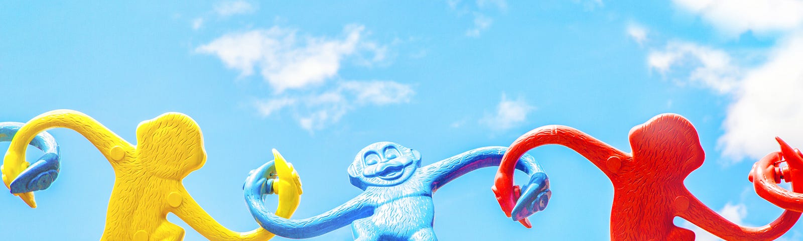3 colorful primary colored monkey game pieces that hook arms for hanging off each other normally are now placed in a horizontal line a float against blue skies as if holding hands in harmony — every monkey’s body/face alternating facing front and back.