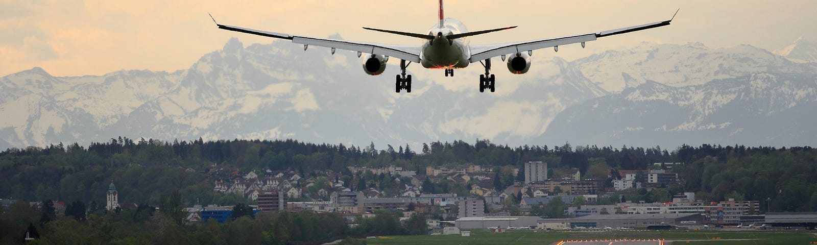 A plane landing not yet set down on the tarmac, runway lights are lit and there is a mountain range in the background.