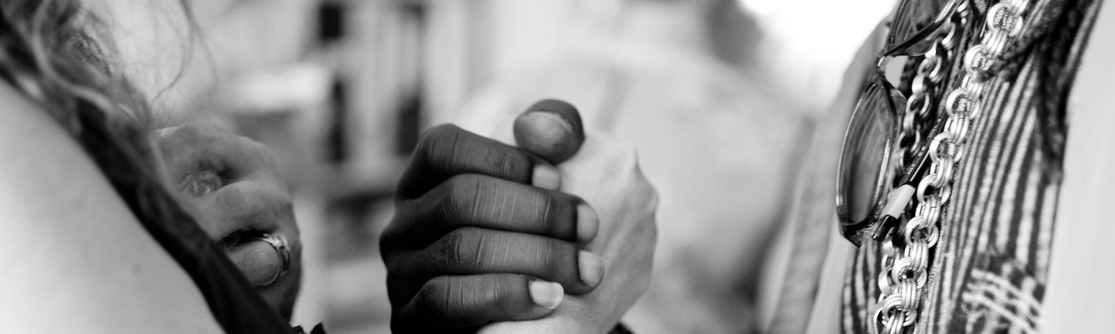 Two people, one white and one black, embracing each other through a unifying handshake