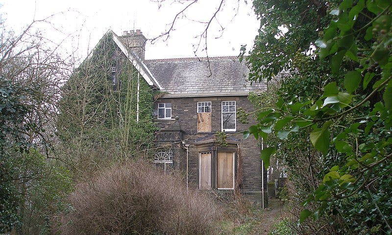 An abandoned, boarded up old house, surrounded by bushes and trees. Very spooky!