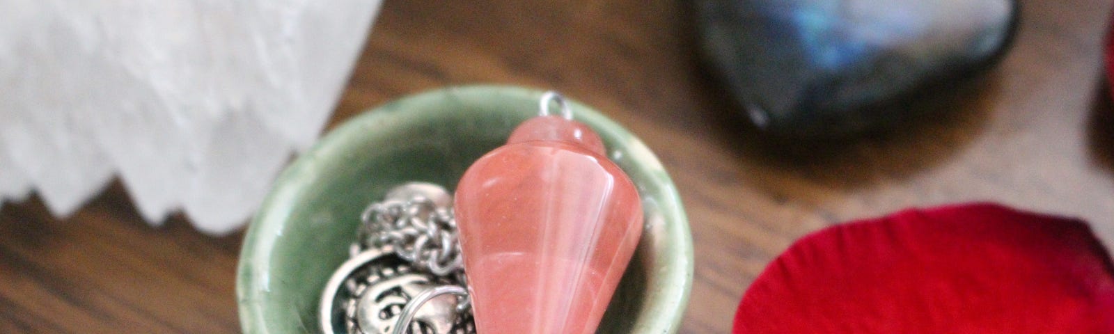 this is a photo of some crystals including a pink pendulum in a bowl.