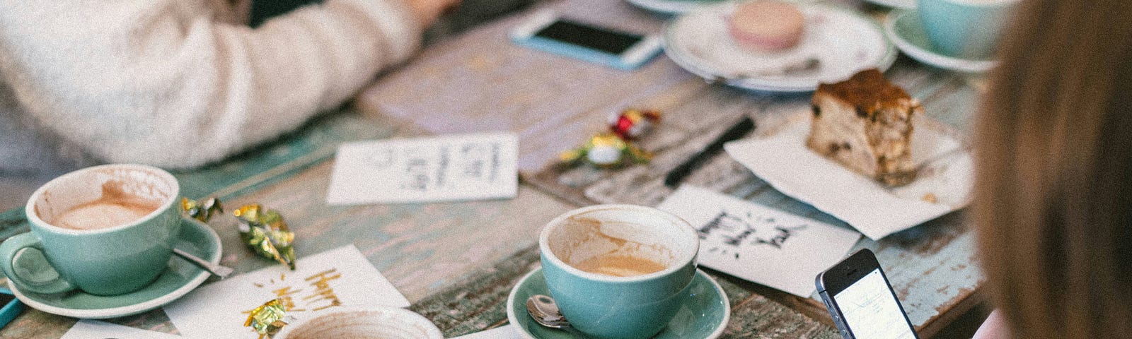 Empty cups and saucers litter a table, surrounded by friends enjoying each other’s company.