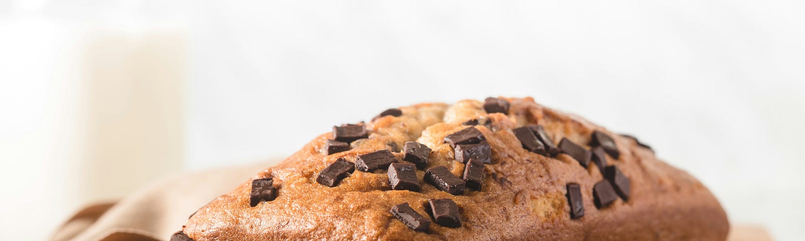 A loaf of choc-chip banana bread sits on a wooden board