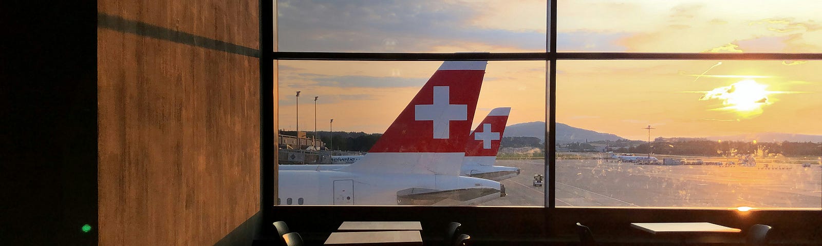 photo of tables in an airport, in front of a window overlooking plane tails