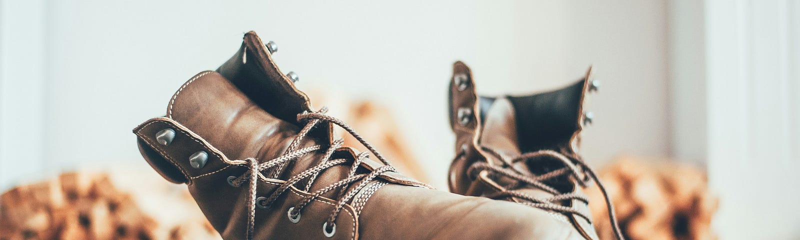 A pair of well worn hiking boots slightly askew. Firewood seen in the background.