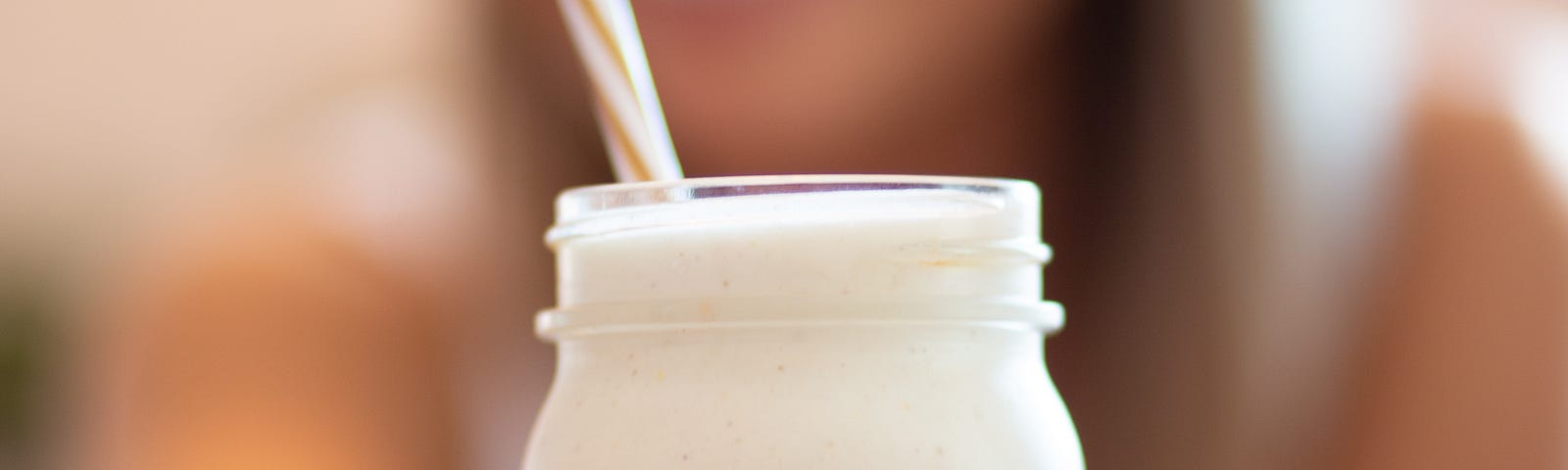 Jar of milk with a straw in it, held by lady whose image is blurred image. Age slower with low-fat cow milk.
