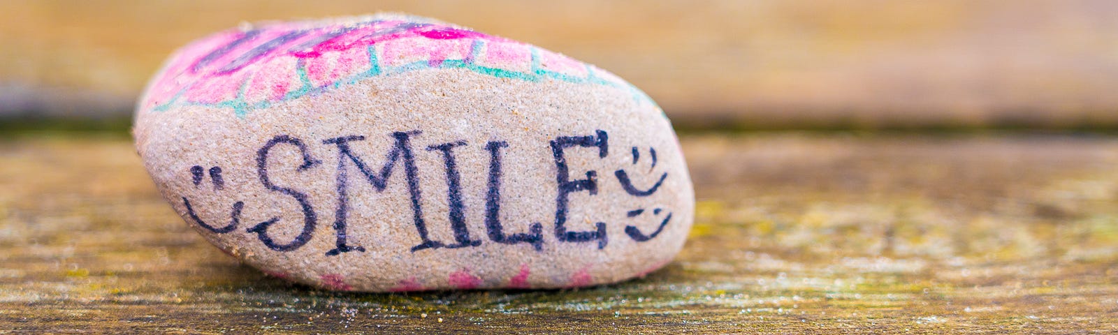 The word smile painted on a rock which is on a wooden table