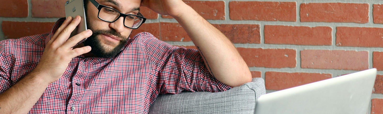 Man is bored while listening on the phone and reading something on his computer.