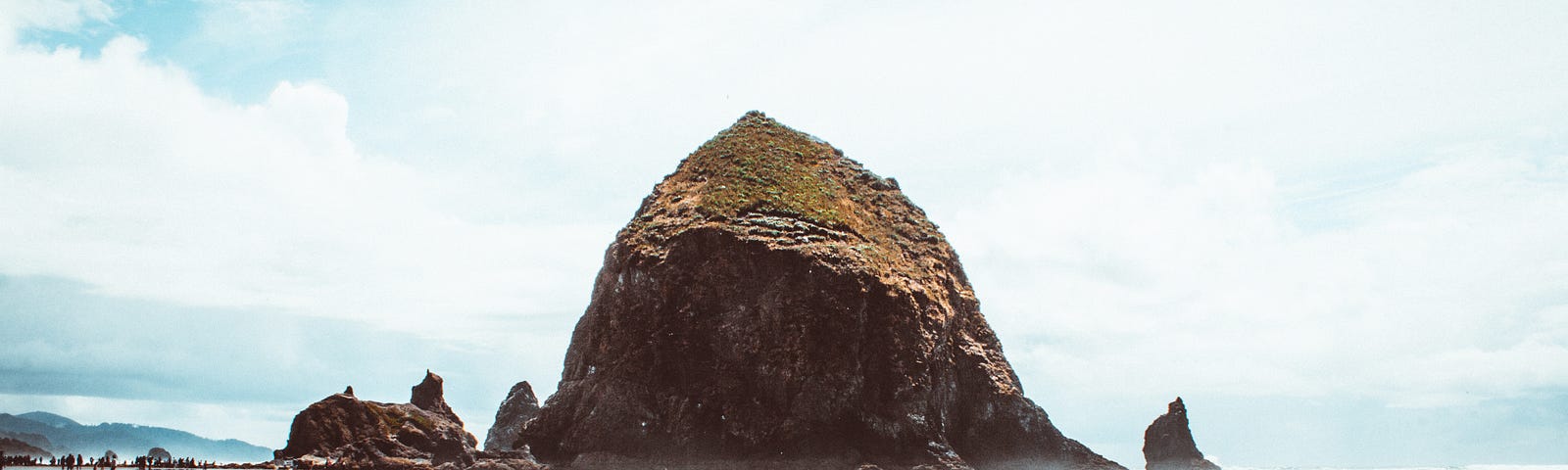 waves at the seashore wash past a large rock which is reflected in the water