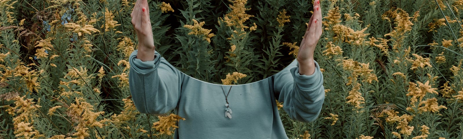 A girl holding a mirror over her face in a field of flowers