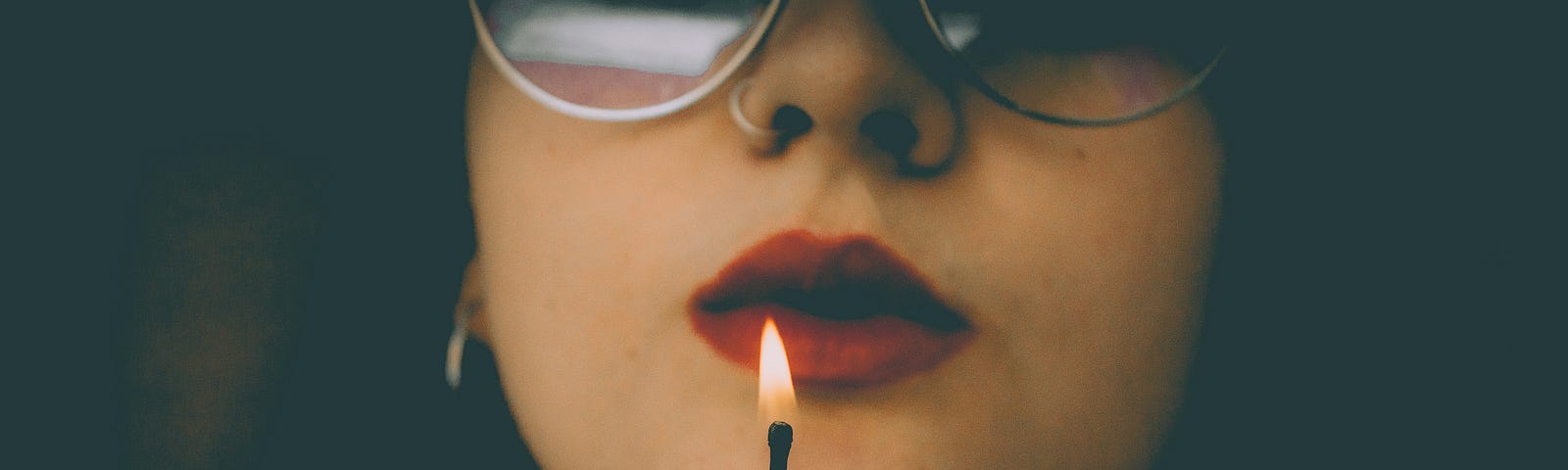 woman in glasses with red lipstick holding a lit match