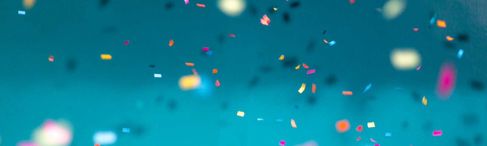 Colorful confetti falling on a blue background, with some pieces in focus and others blurred