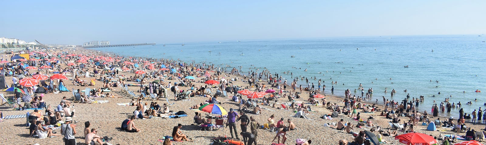 Crowds on Brighton beach and in the sea, on a hot day with a cloudless sky in the UK.