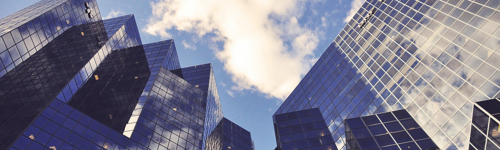 glass-paneled skyscrapers below a blue sky with clouds