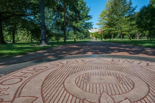 A view of the Ohio State Oval, with the university seal in the foreground. In the distance, the top of Thompson Library.