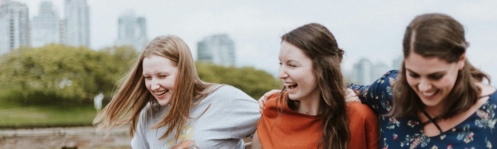 Three mom friends laughing, walking arm in arm in the park.