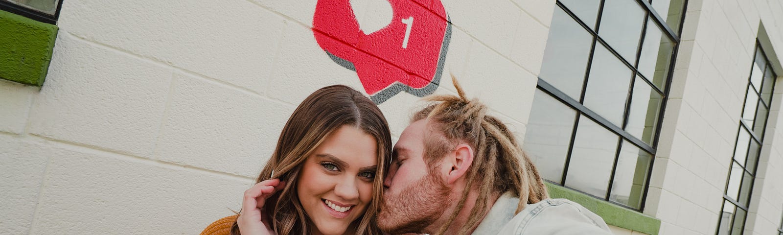 man with dreadlock kissing woman on the cheek while taking a selfie