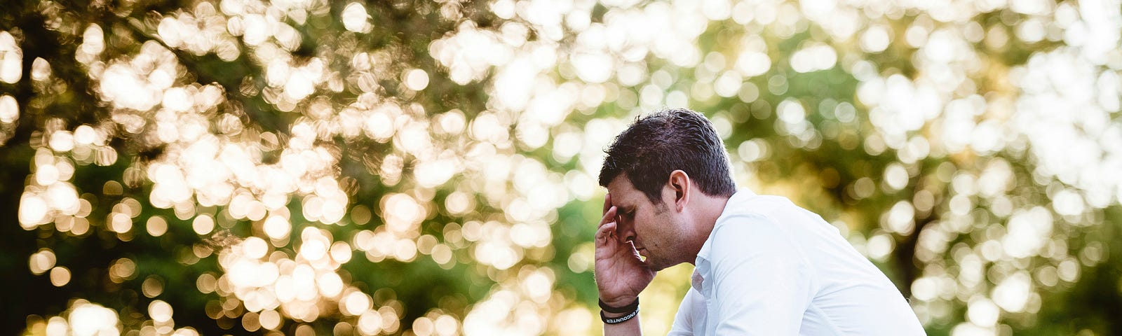 Man sitting on piece of log by himself and looking stressed.