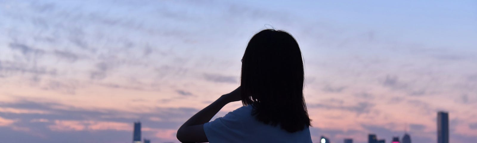 girl sitting otuside in the evening by the water and a city