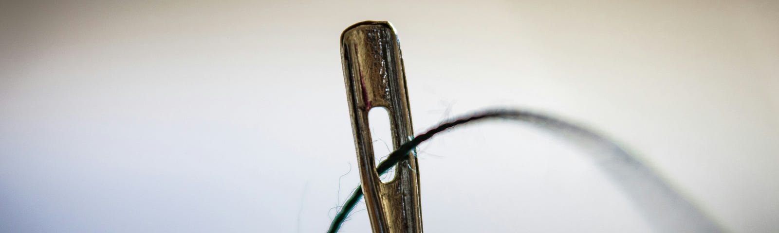 Closeup photo of the eye of a needle, with thread going through