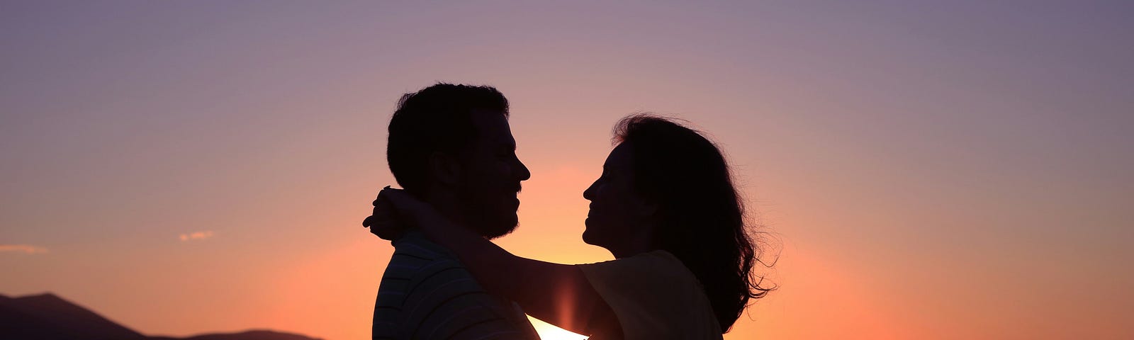 Couple hugging and smiling at each other with the sunset in the background