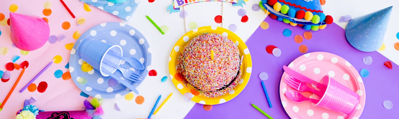 A birthday sign, cake, party hats, and confetti lay across a table