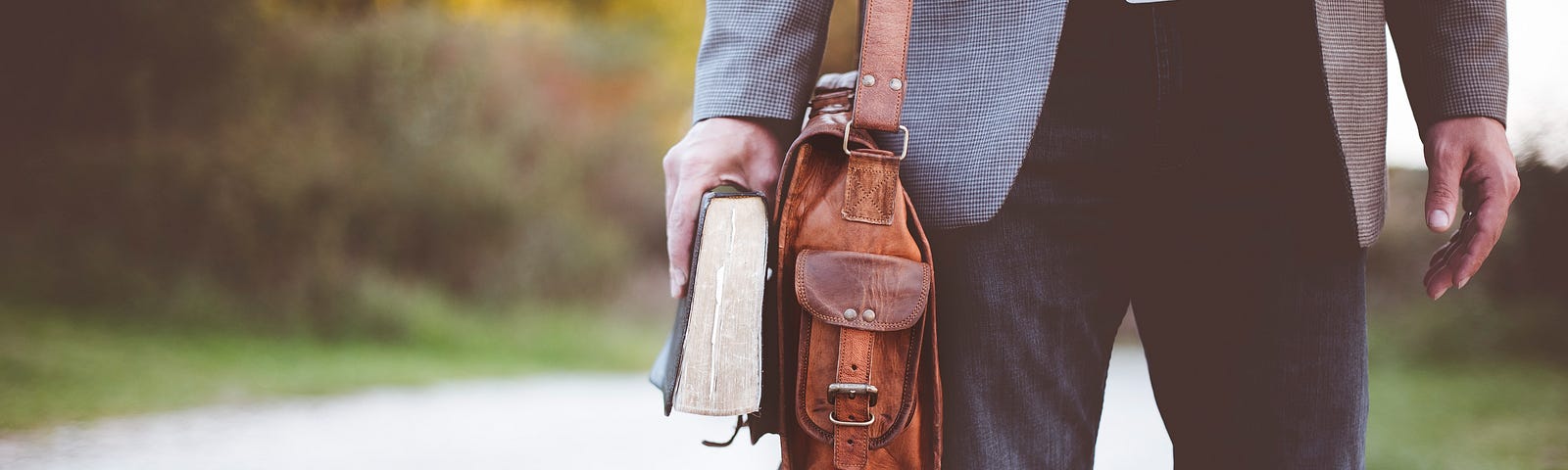 Man walking a path with a brown leather satchel and a Bible
