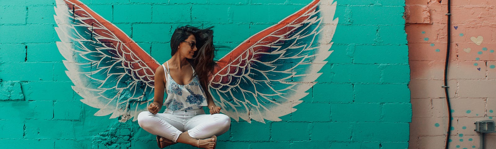 woman levitating in front of a wall with wings