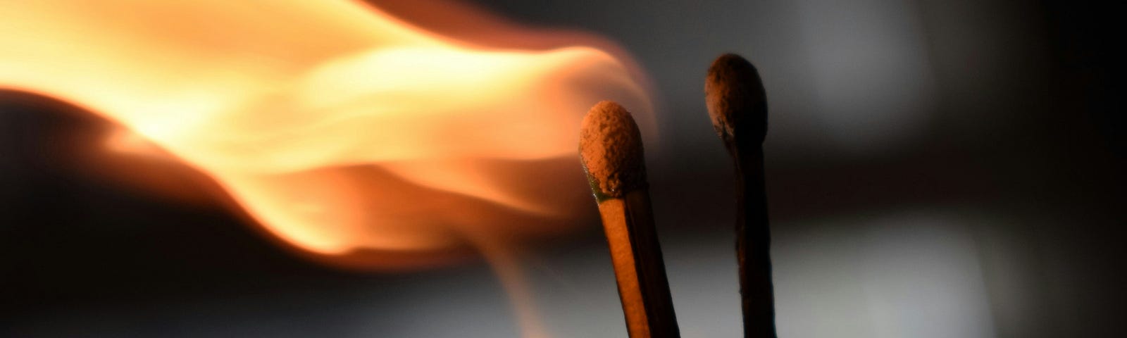 Photo of two matches against a blurry background. One match is burnt, and the other one is burning.