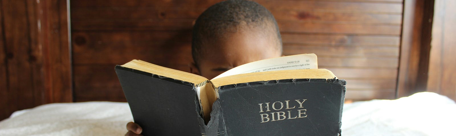 Young boy reading a bible in bed.