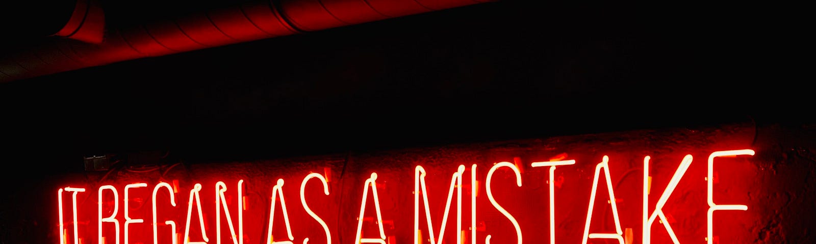 Red neon sign that reads “IT BEGAN AS A MISTAKE”.