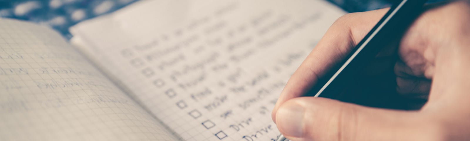 Hand holding pen over grid notepad with a to-do list. Pen poised to add another item